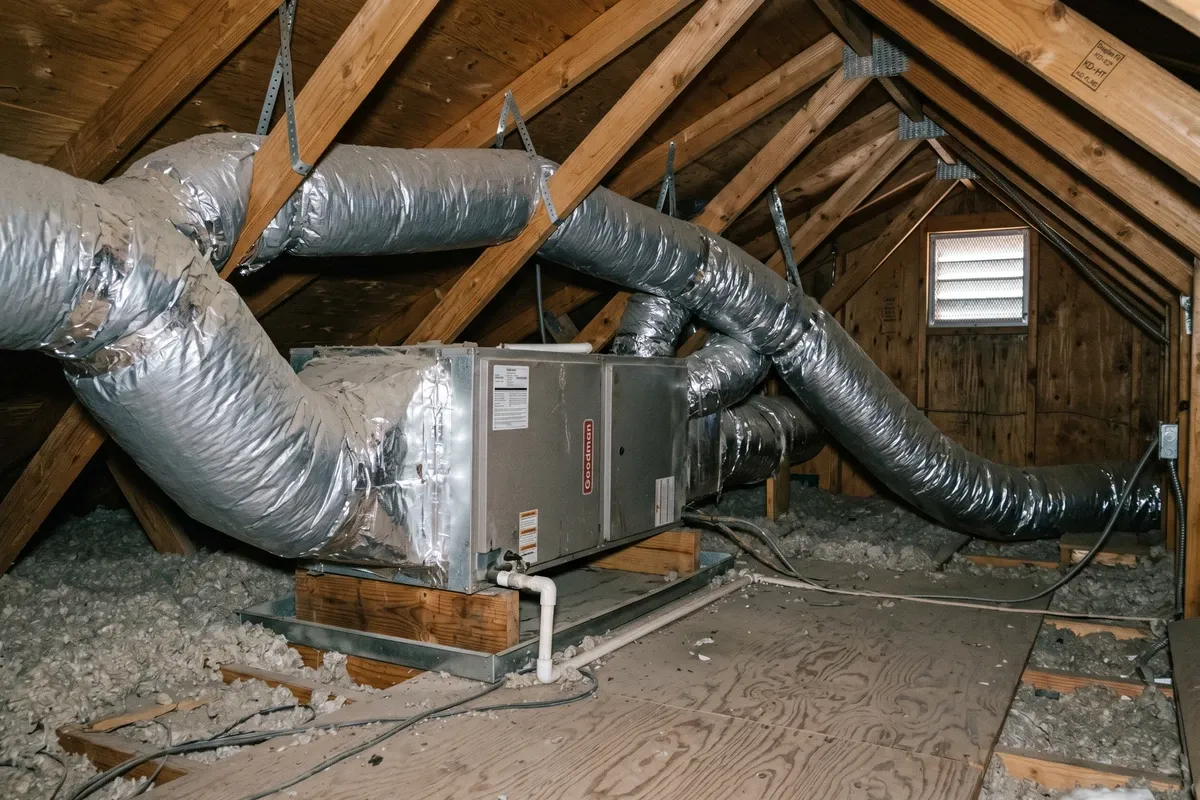 Attic space in a Phoenix home with AC air handler unit and ductwork visible, dusty attic environment, diffuse light, no faces.