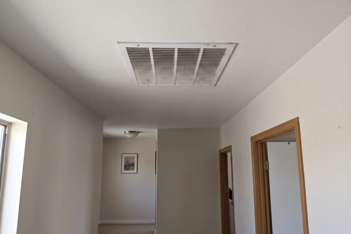 Ceiling air grille in a hallway of a Phoenix home with a light layer of dust on the slats