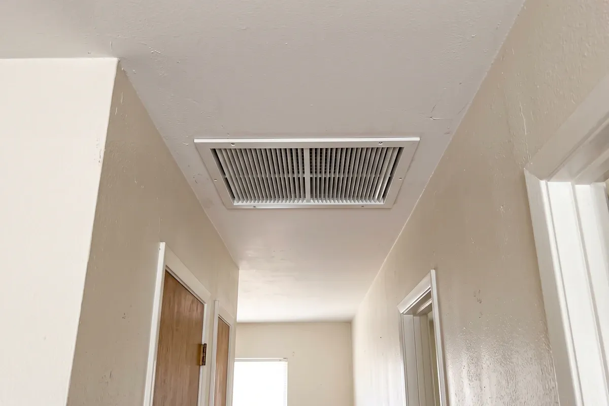 A white louvered ceiling air grille in a plain hallway, with no stains or visible growth around it