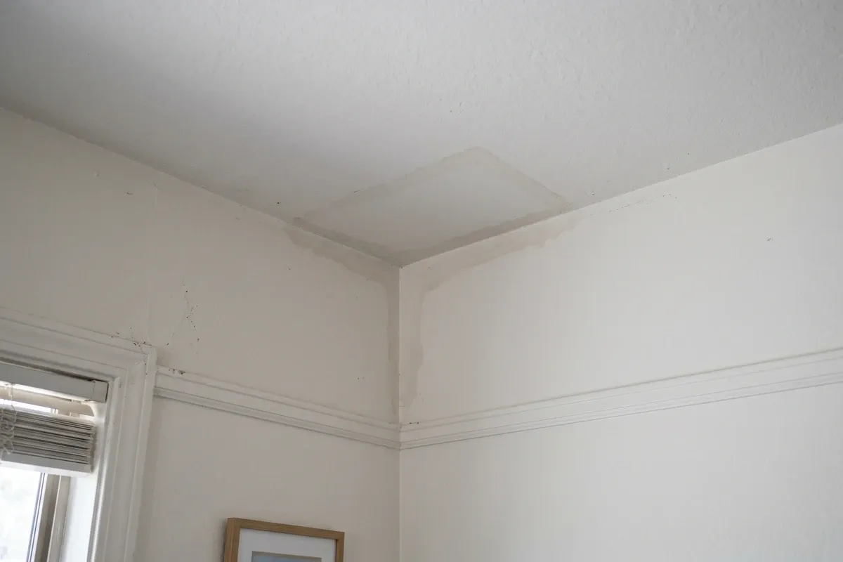 Faint brown water stain spreading from the wall-ceiling junction in a Phoenix home interior, early moisture mark on white drywall from a slow AC or roof leak above.