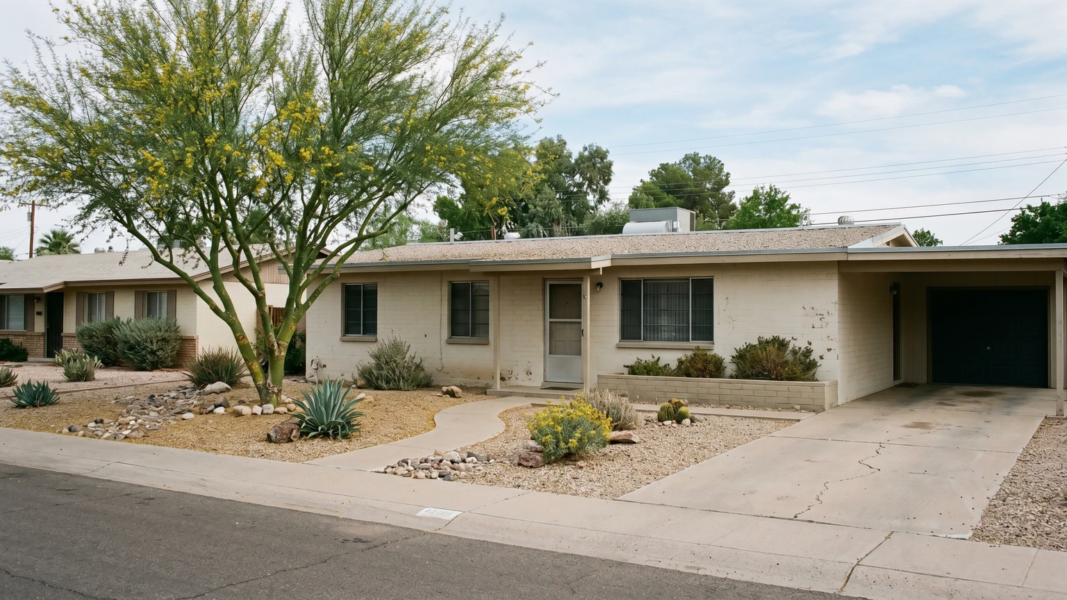 A single-story stucco ranch home from the 1960s on a quiet Phoenix street, mature desert landscaping, aged stucco, natural afternoon light.